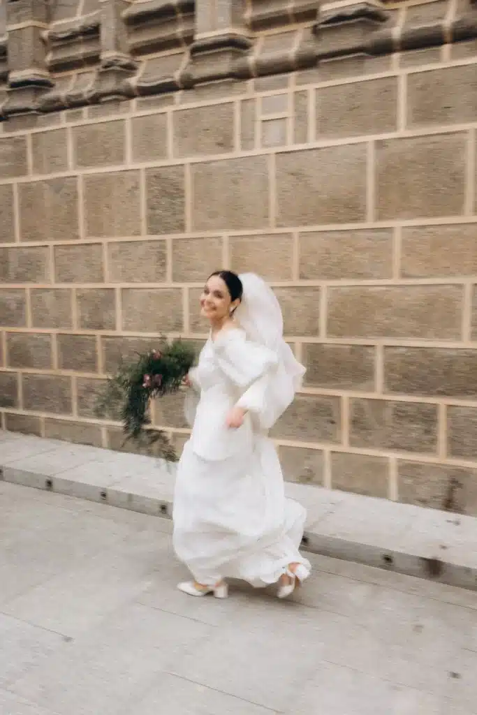 Joyful bride running outside stone venue during wedding in Spain
