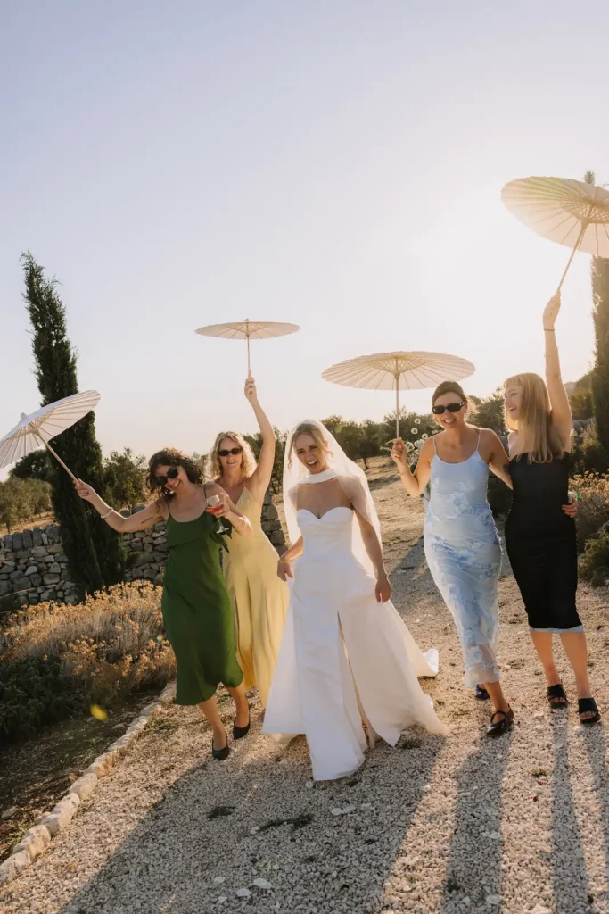 Bride walking with her bridesmaids under parasols during a destination wedding in Sicily